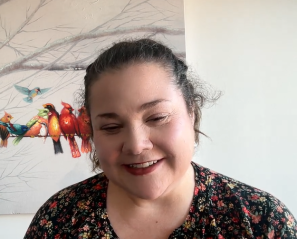 Woman with dark hair smiles on zoom screen with picture or birds behind
