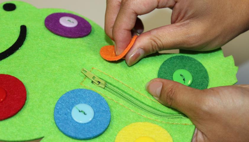 A hand unbuttoning one of the buttons on a felt frog. 