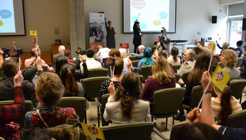 The audience waves flags in a show of support to engage in more positive conversations between health care providers and kids with disabilities after the first research panel’s presentation.