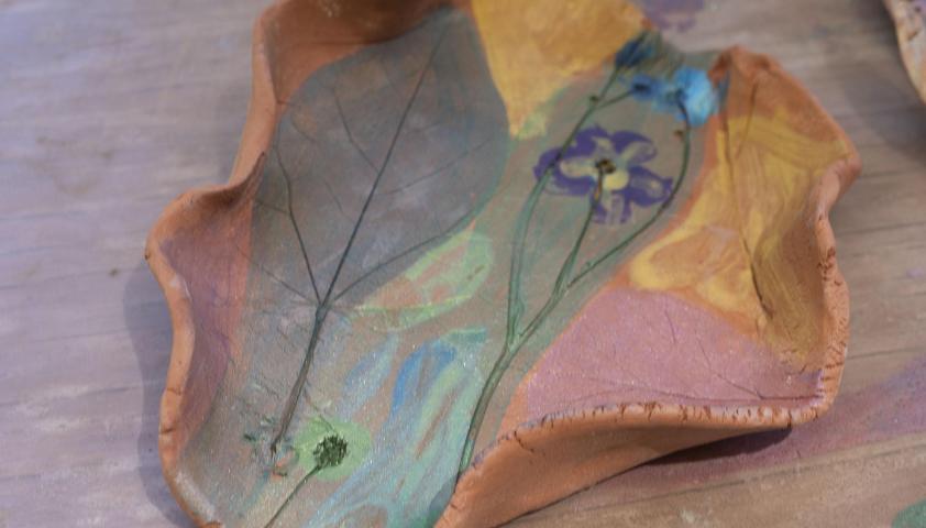 clay art project that is multi-coloured blue and red and shaped like an abstract shell, with flowers painted on.