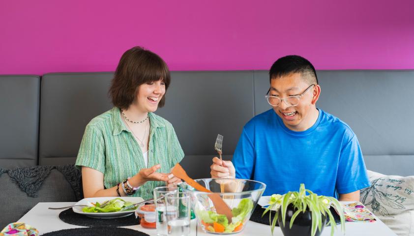 Nick and a friend smiling while sharing a meal together. 