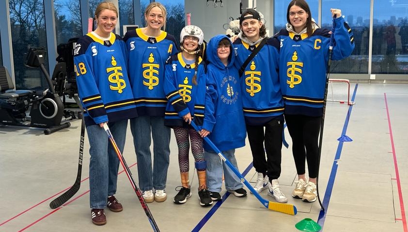 A child standing and smiling with hockey players.