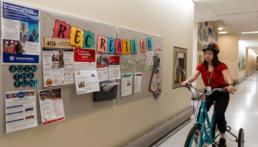 A young woman riding a bike through the hallways of Holland Bloorview.