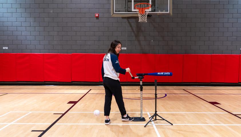 A young woman setting up a baseball activity in an indoor gym.