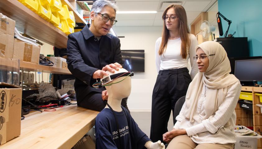 Three adults having a conversation while interacting with a brain computer interface on a child mannequin.