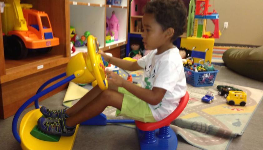 A boy with medium skin tone playing with a toy sled in the playroom.