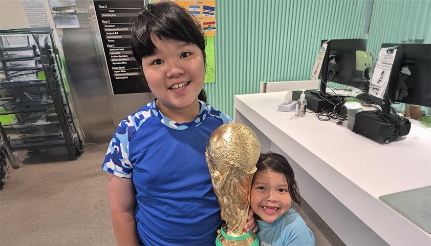 Two children are holding up a FIFA World Cup trophy