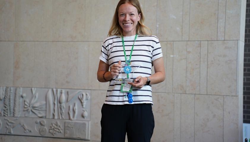 A clinician holding an award on a stage against a beige wall
