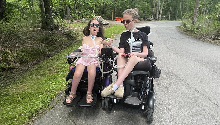 Two teenagers on wheelchairs are enjoying outdoor activities