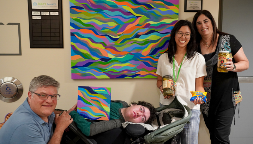 group of adults pose in front of colourful artwork and a plaque