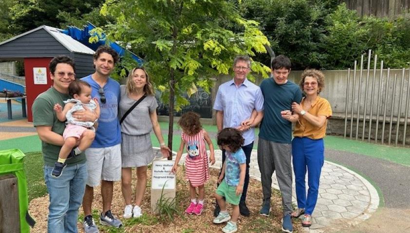 A group of adults and kids stand outdoors beside a tall tree