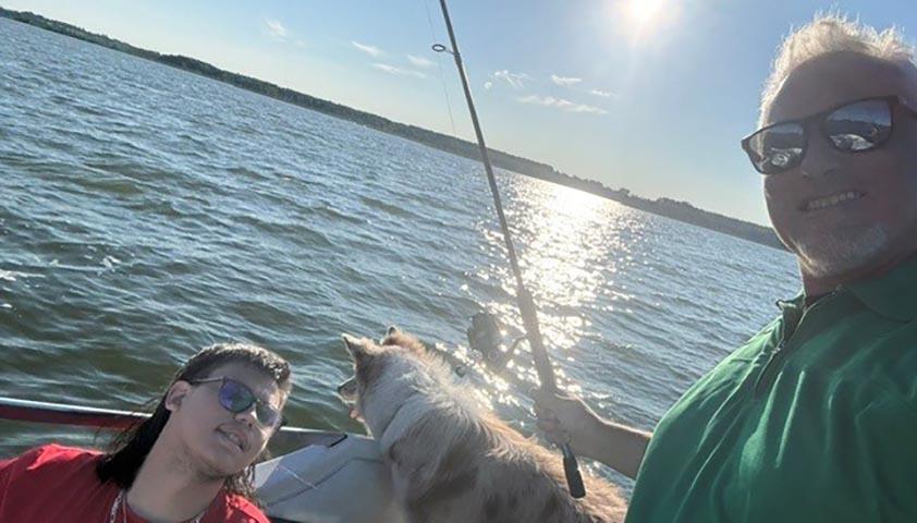 An adult is on a boat with a teenager and a dog, fishing
