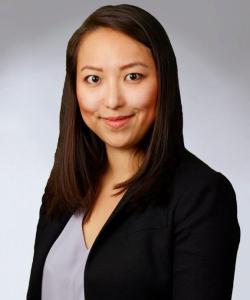 An adult with medium skin tone, long brown hair wearing a black blazer and grey top.