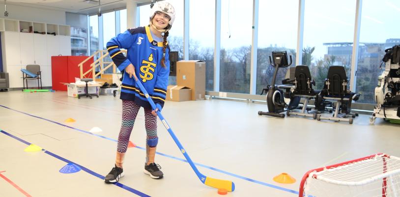 A child holding a hockey stick in front of a hockey net, wearing a helmet and ankle brace.