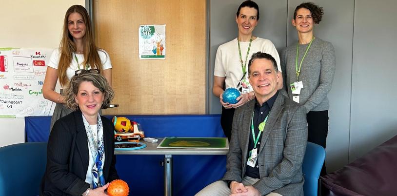 group of adults, some sitting and others standing, in a room with bubble towers in the background