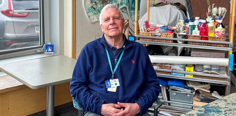A man sits in an art therapy room with his hands in his lap. 
