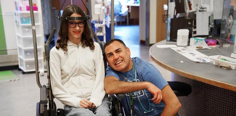 An adult with a teenager who is sitting on a wheelchair
