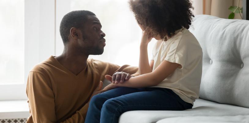 Young girl on couch being consoled by man.
