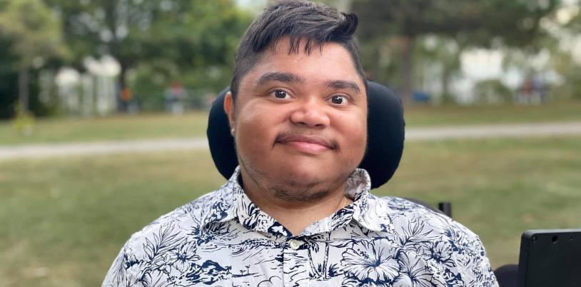 Man with dark hair in wheelchair smiles in park