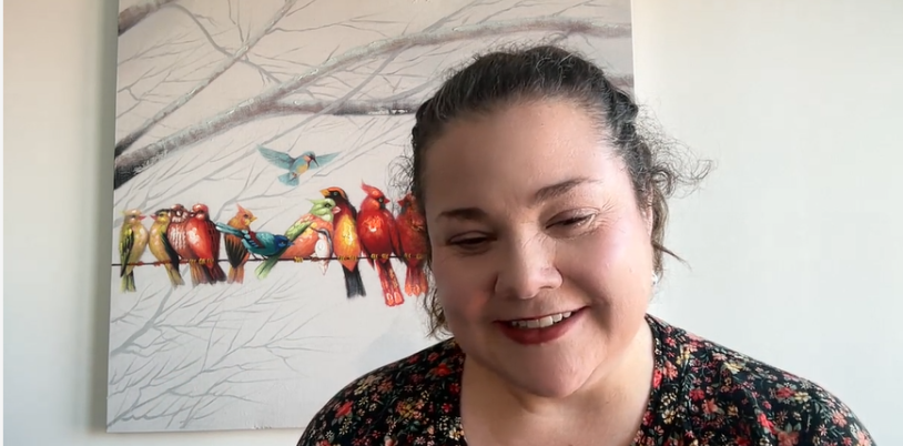 Woman with dark hair smiles on zoom screen with picture or birds behind