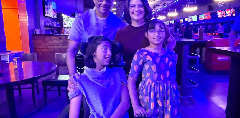 Girl in wheelchair with another girl beside her and man and woman behind in bowling alley