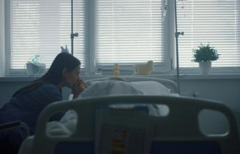 Mother with long black hair reaching over hospital bed to patient