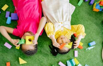 Two young children lie on the floor and play with blocks