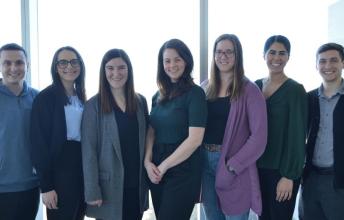 A group of researchers smile as they stand together in front of a brightly-lit window.