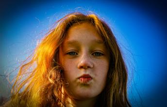 Girl with red hair purses lips on blue background