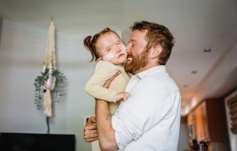 Man with beard hugs small girl with pony tails and nasal prongs
