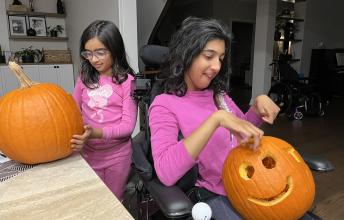Two girls with pink shirts carve pumpkins