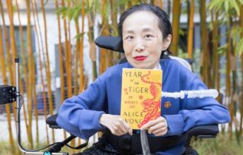 Woman in royal blue holding book called Year of the Tiger sits in wheelchair