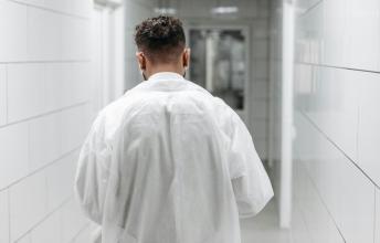 Man in white doctor's coat walks down hospital hall