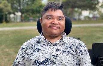 Man with dark hair in wheelchair smiles in park
