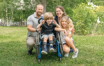 Boy outside in wheelchair beside girl with man and woman behind