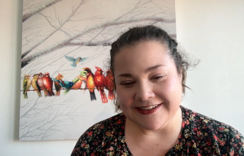 Woman with dark hair smiles on zoom screen with picture or birds behind