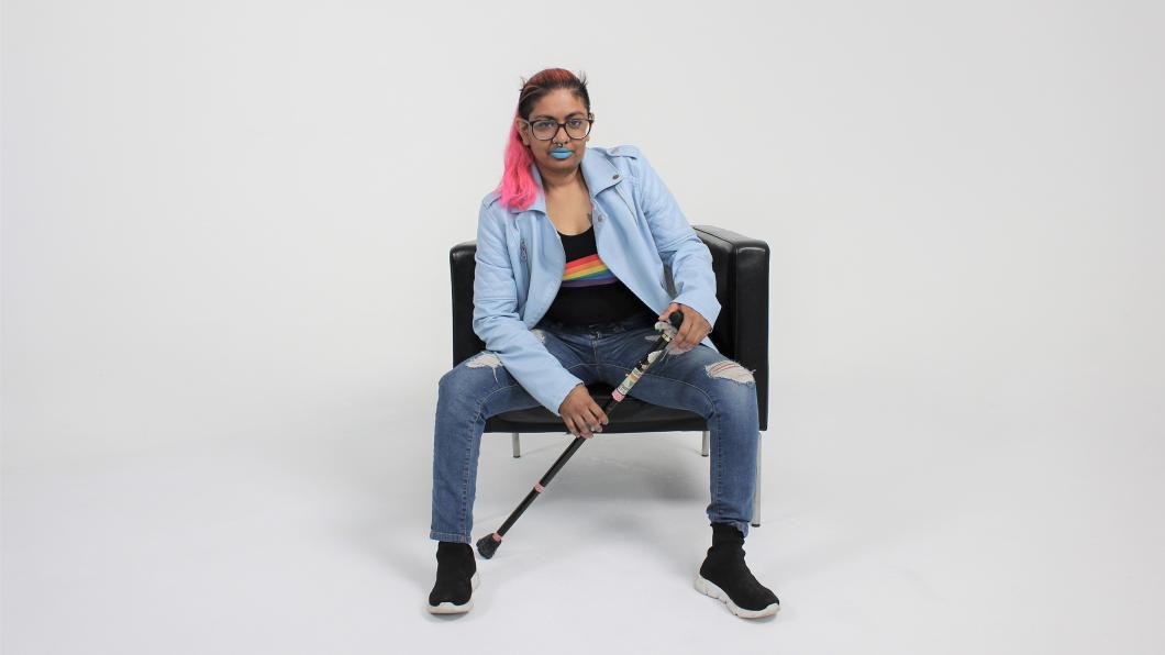 Brown woman wearing a rainbow shirt and jeans with pink ponytail and cane