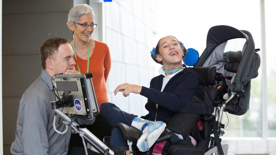 Teen girl in wheelchair with a communication system beside two adults