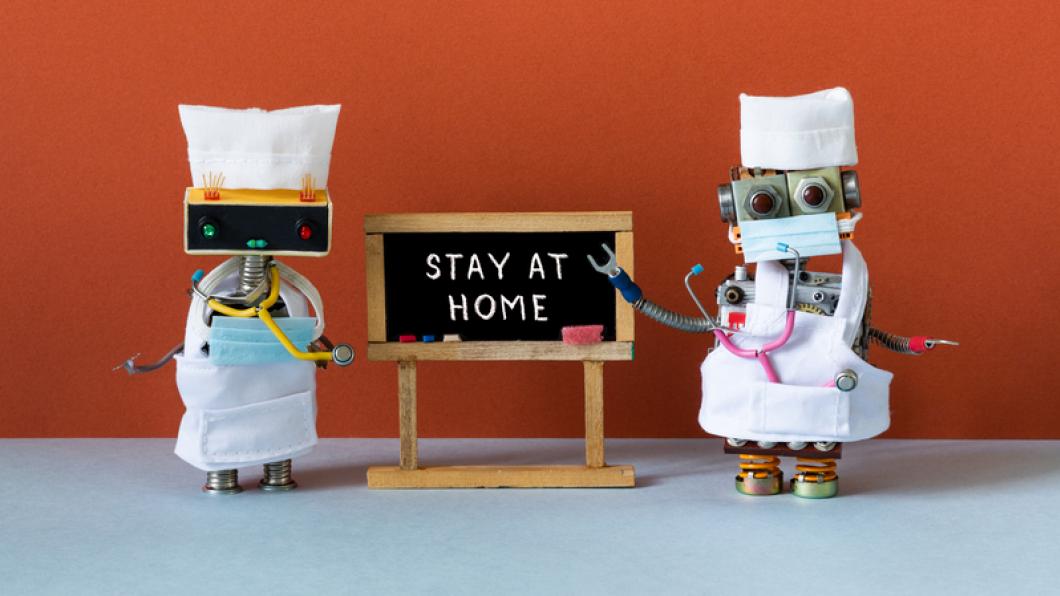 Two robots dressed as doctors with Stay at Home sign