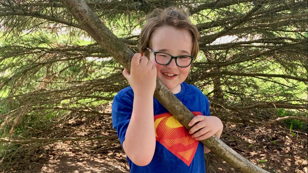 Wesley in a Superman shirt holding up a large branch.