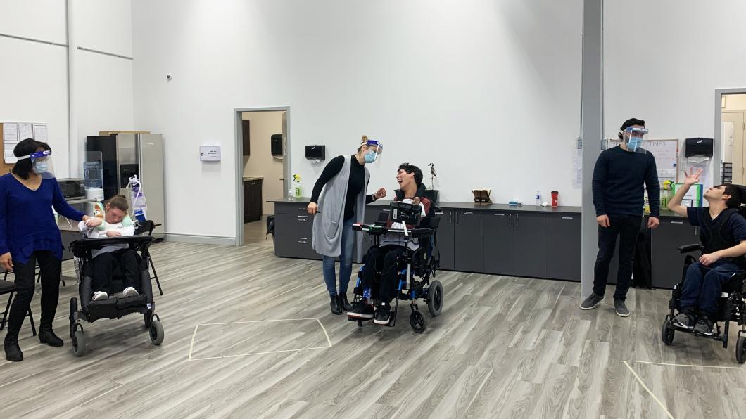 Three young adults in wheelchairs with staff wearing masks and shields