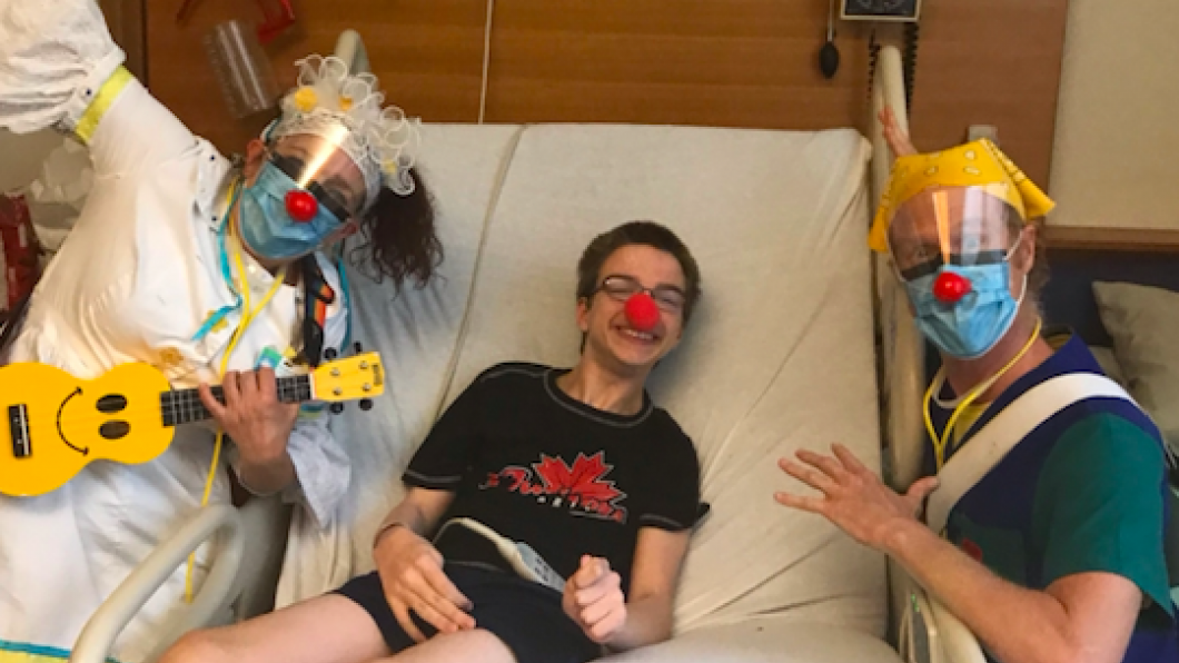 Andrew in bed with a red nose, with the therapeutic clowns posing by his bedside.