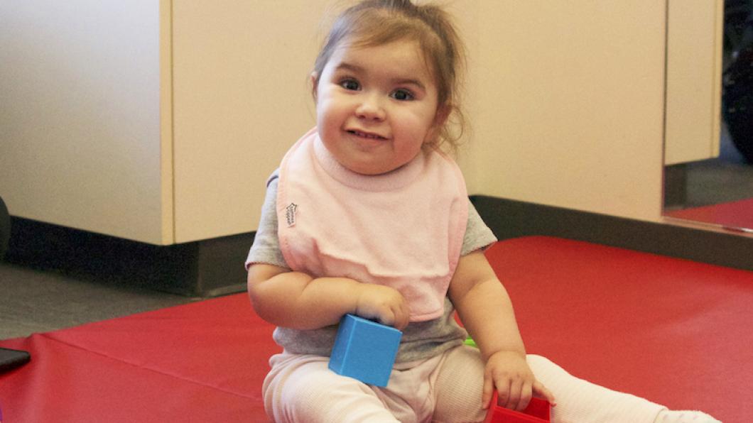 Toddler girl on red mat with toys