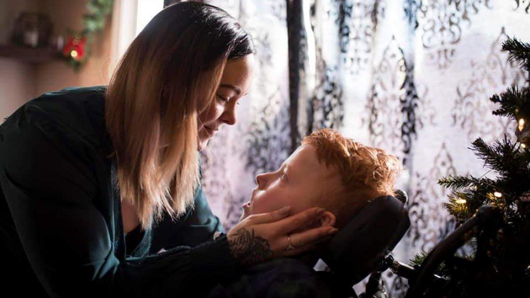 Boy in wheelchair with mom leaning down and holding his face