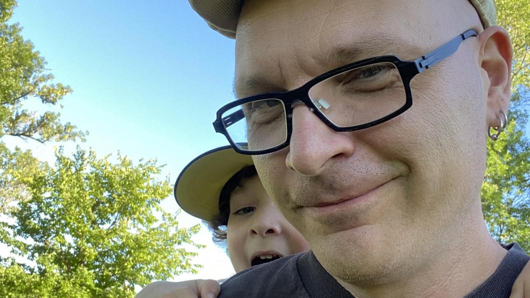 Man with glasses and cap and small boy learning over his shoulder