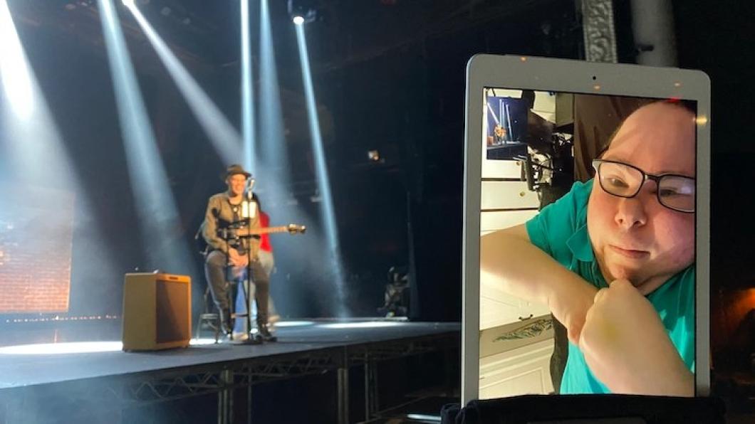 Image of man's face on Ipad screen with background of a singer on a stage