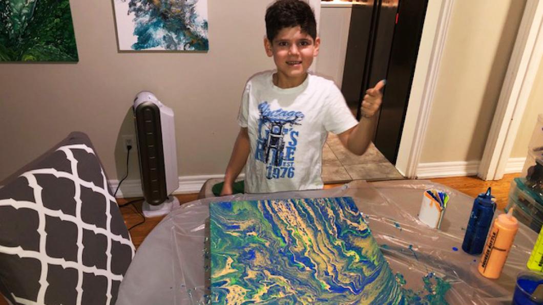 Boy at table with abstract painting and paint bottles