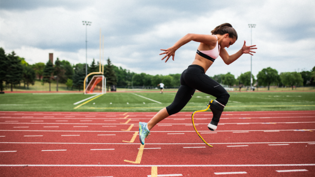 A young woman running on a track. She is wearing a running blade on her right leg, black leggings and a pink top.