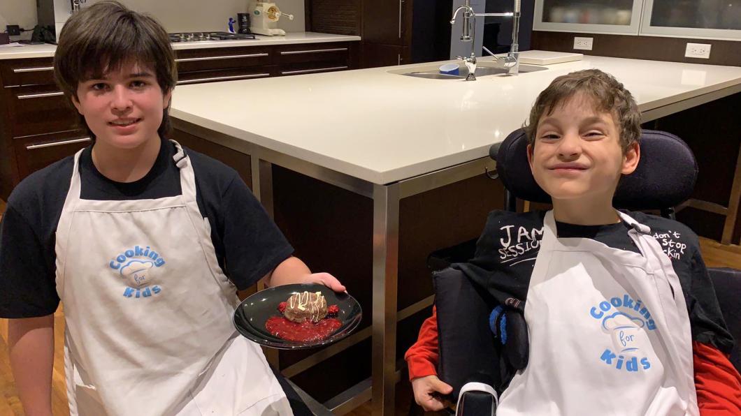Two boys in aprons with one holding a piece of chocolate lava cake