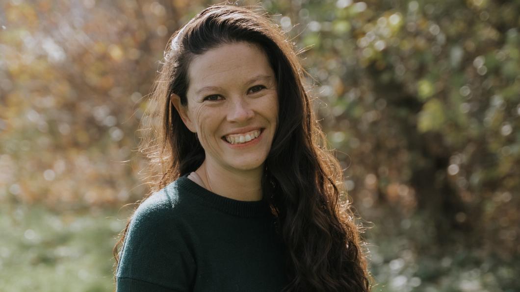 Young woman with long hair smiles with nature behind